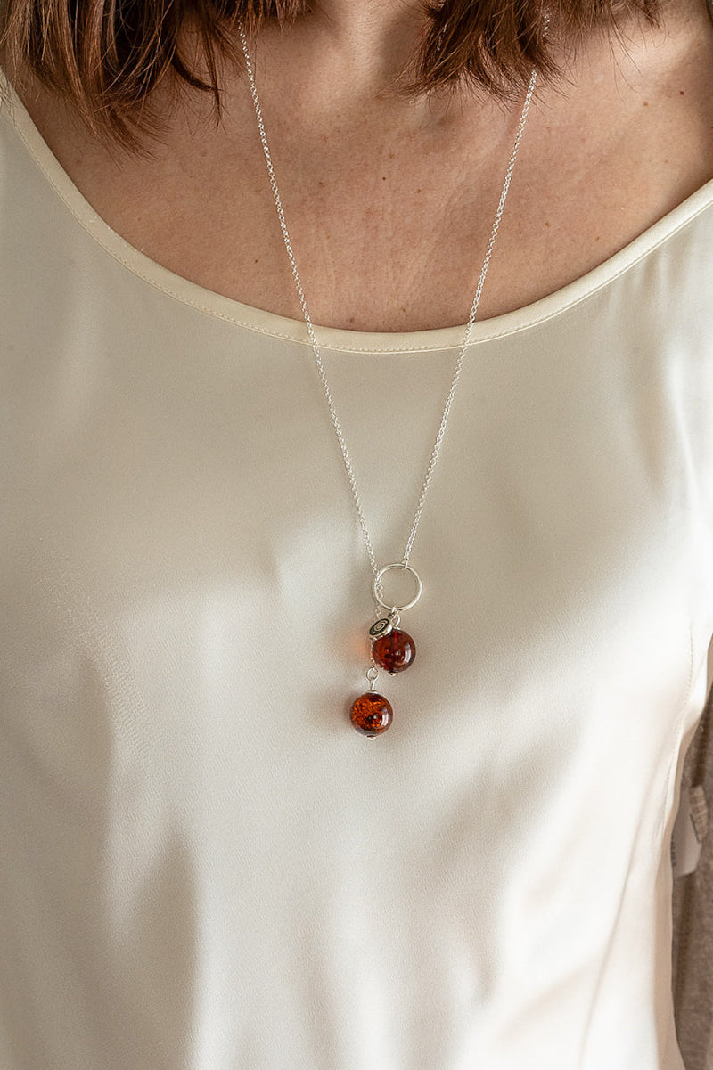 Necklace with amber beads worn by a person on a plain background