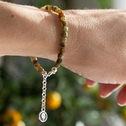 Bracelet with green and orange beads on a wrist against a blurred natural background
