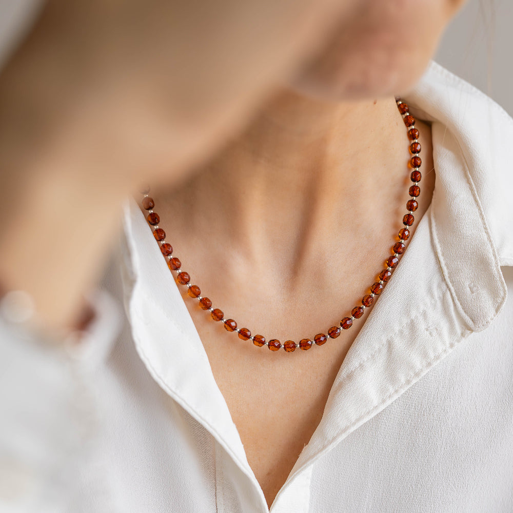 Person wearing a white shirt with a red amber beaded necklace