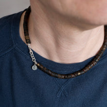 Load image into Gallery viewer, Close-up of a person wearing a dark blue shirt with a Baltic amber necklace featuring wooden beads and a silver chain.