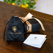 Load image into Gallery viewer, Lina Snara jewelry packaging with black drawstring bag, box, and card on a wooden surface.